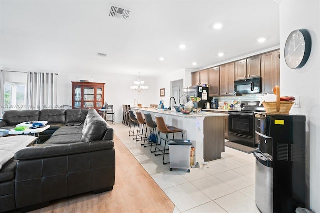 kitchen featuring hanging light fixtures, black appliances, tasteful backsplash, an island with sink, and a kitchen breakfast bar