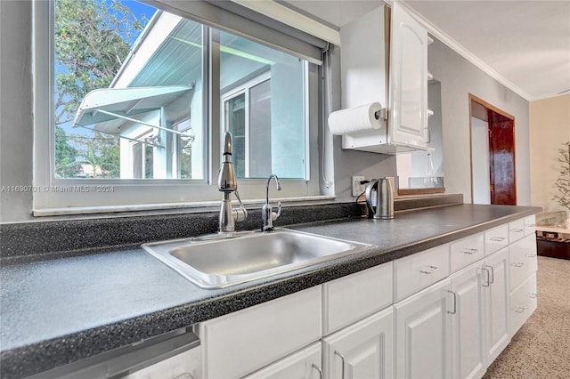 kitchen with dishwasher, white cabinets, crown molding, sink, and a skylight