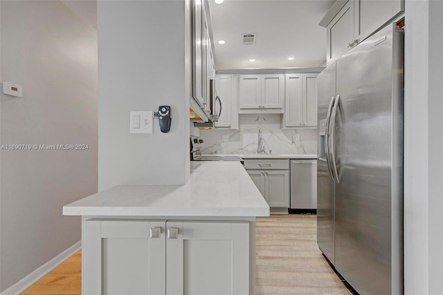 kitchen featuring light hardwood / wood-style floors, sink, kitchen peninsula, appliances with stainless steel finishes, and tasteful backsplash