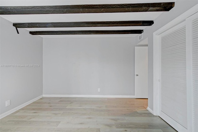 spare room featuring light wood-type flooring and beam ceiling