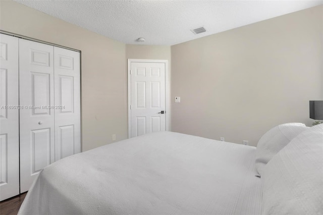 bedroom with dark hardwood / wood-style floors, a textured ceiling, and a closet