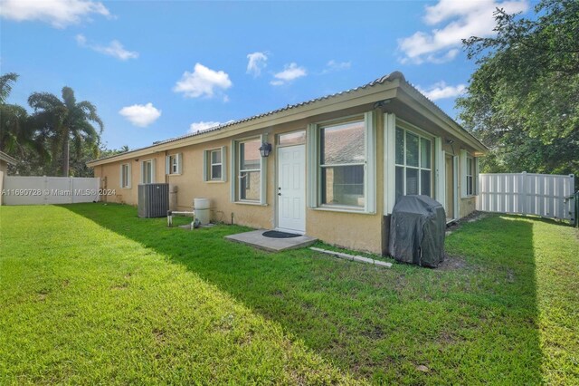 rear view of house with central AC unit and a yard