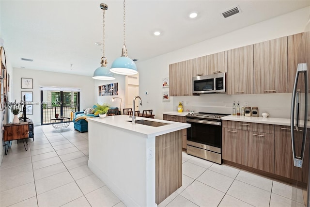 kitchen with a center island with sink, appliances with stainless steel finishes, decorative light fixtures, light tile patterned floors, and sink