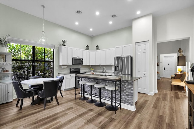 kitchen with a kitchen bar, a center island with sink, a towering ceiling, light wood-type flooring, and appliances with stainless steel finishes