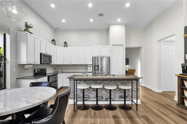 kitchen with stainless steel appliances, white cabinetry, a kitchen breakfast bar, light hardwood / wood-style floors, and a kitchen island with sink