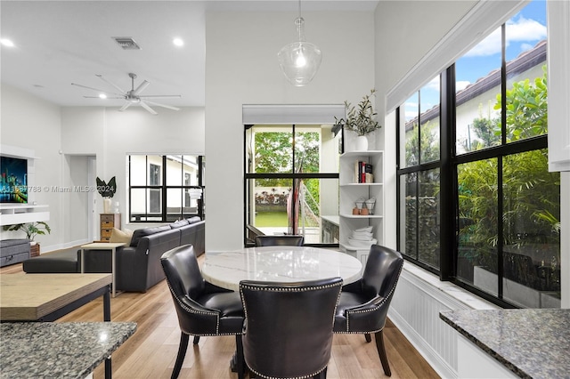 dining space featuring light wood-type flooring, ceiling fan, and a high ceiling