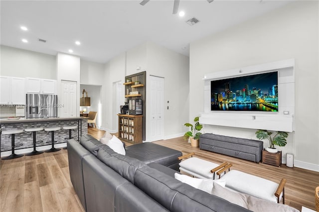 living room with a high ceiling, ceiling fan, and light hardwood / wood-style floors