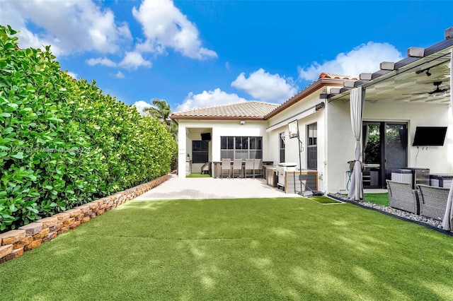 rear view of property featuring ceiling fan, a lawn, area for grilling, and a patio area