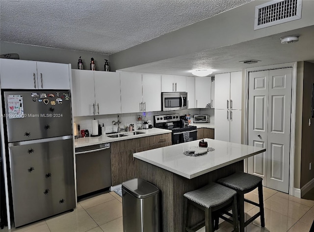 kitchen with stainless steel appliances, sink, a kitchen island, a breakfast bar, and white cabinetry