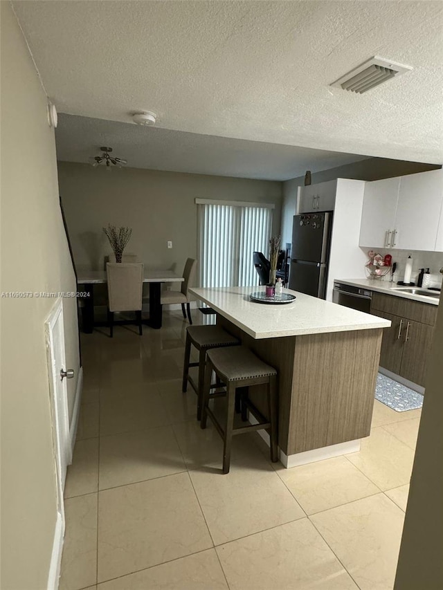 kitchen with stainless steel appliances, a center island, white cabinets, a textured ceiling, and light tile patterned floors