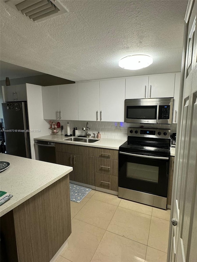 kitchen with stainless steel appliances, dark brown cabinetry, sink, light tile patterned floors, and white cabinetry