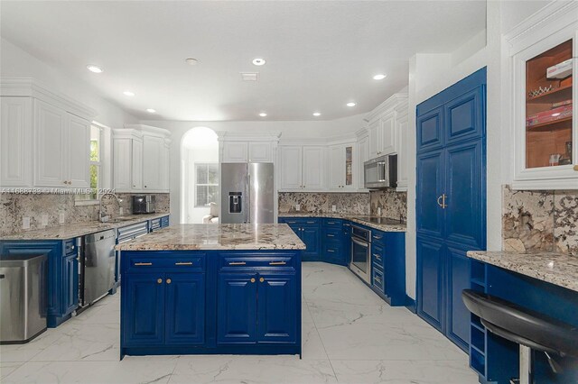 kitchen featuring sink, appliances with stainless steel finishes, blue cabinetry, a kitchen island, and white cabinets