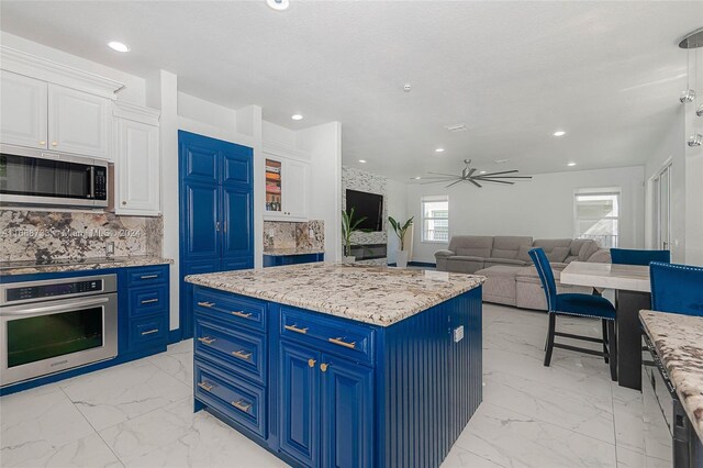 kitchen featuring a center island, blue cabinets, ceiling fan, white cabinetry, and appliances with stainless steel finishes