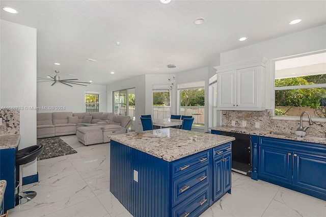 kitchen featuring white cabinetry, sink, light stone countertops, a kitchen island, and blue cabinets