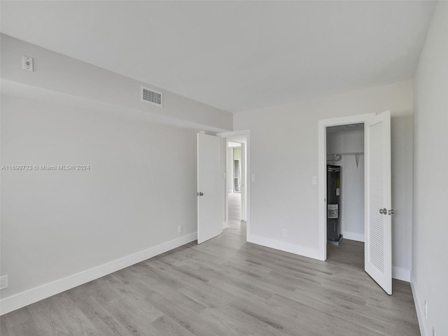 unfurnished bedroom featuring water heater, a closet, a spacious closet, and light hardwood / wood-style floors