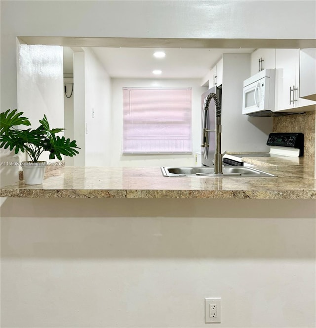 kitchen featuring sink, light stone counters, stove, and white cabinets