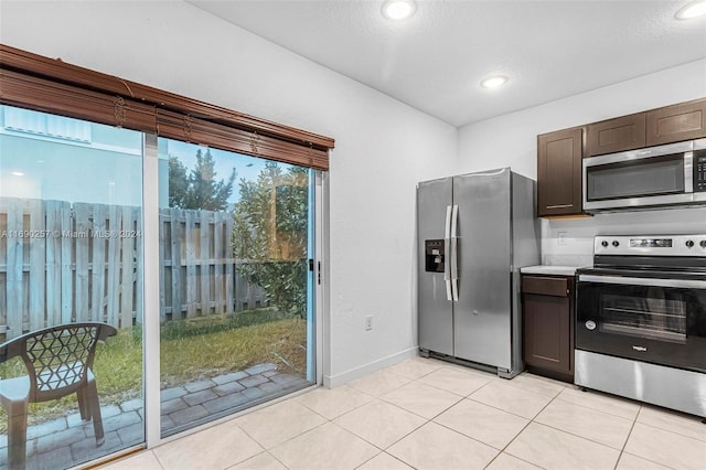 kitchen with a textured ceiling, dark brown cabinetry, light tile patterned floors, and stainless steel appliances