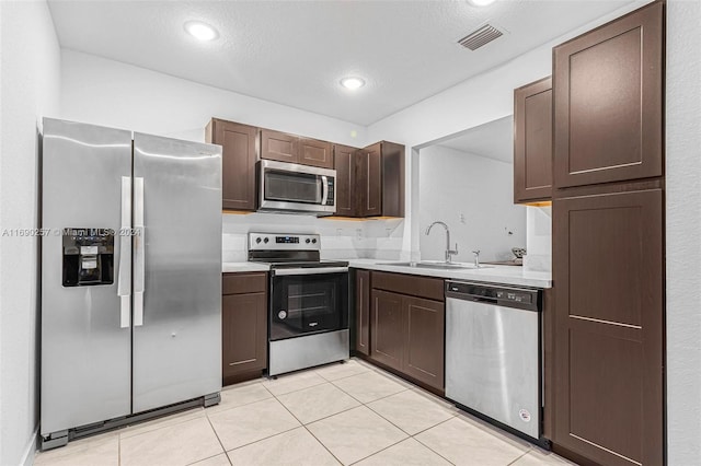 kitchen with light tile patterned flooring, stainless steel appliances, a textured ceiling, dark brown cabinetry, and sink