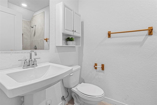 bathroom with toilet, sink, and tiled shower