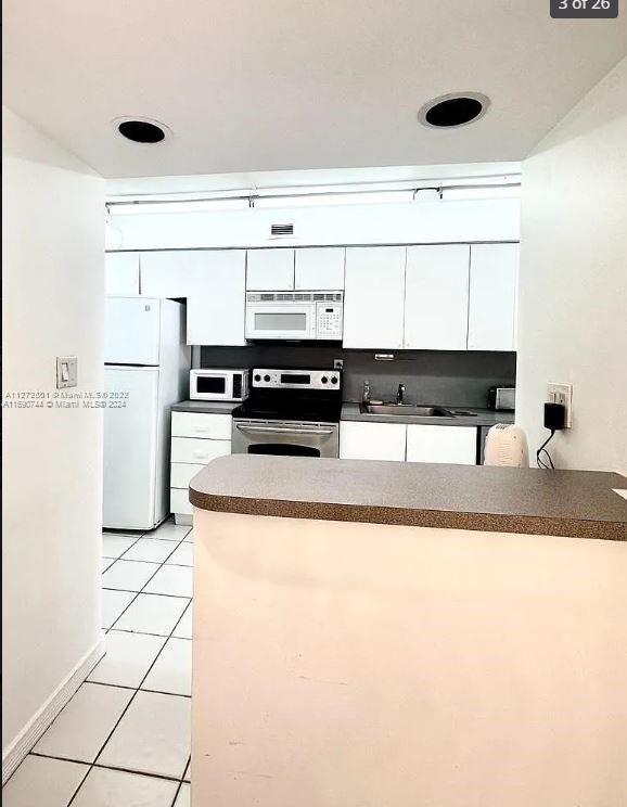 kitchen featuring white appliances, sink, light tile patterned floors, and white cabinets