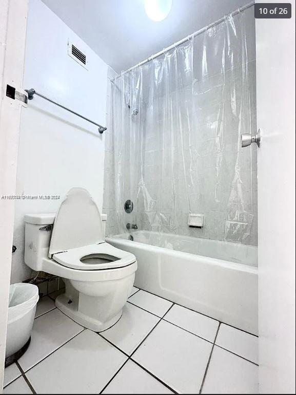 bathroom with tile patterned floors, shower / bathtub combination with curtain, and toilet