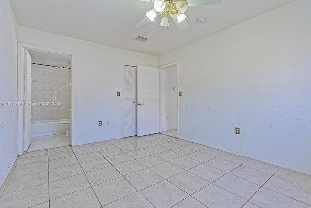 unfurnished bedroom with light tile patterned floors, connected bathroom, a closet, and ceiling fan