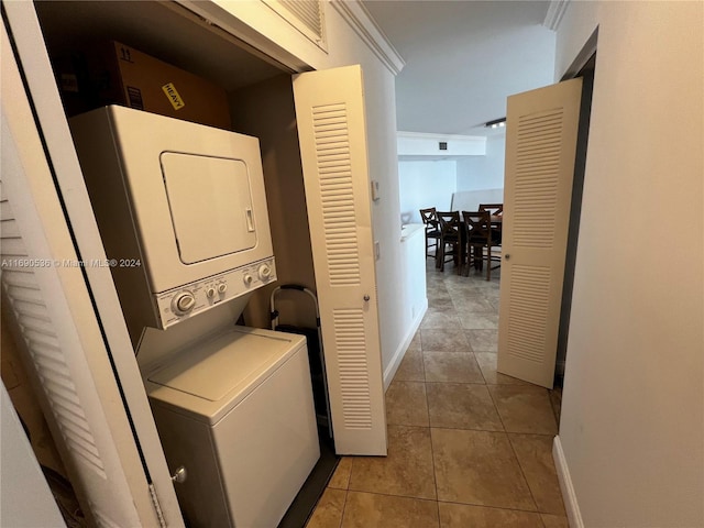 clothes washing area featuring stacked washing maching and dryer, light tile patterned floors, and crown molding