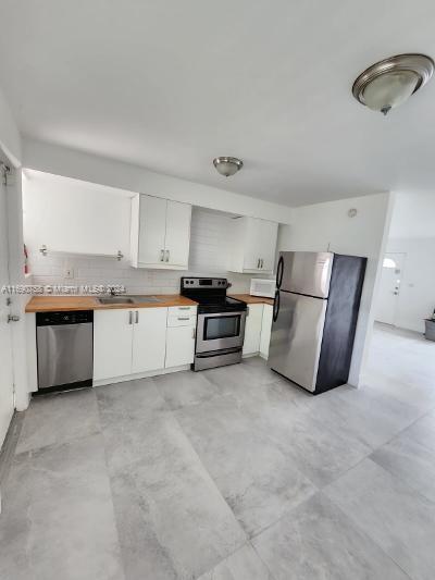 8960 NE 2nd Ave, El Portal, FL 33138 - kitchen featuring stainless steel appliances, wooden counters, white cabinets, and decorative backsplash