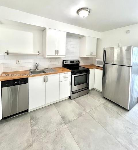 kitchen with butcher block counters, sink, appliances with stainless steel finishes, tasteful backsplash, and white cabinets