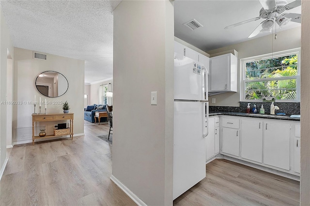 kitchen with sink, white fridge, a textured ceiling, white cabinets, and light wood-type flooring