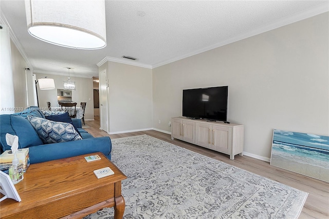 living room with a notable chandelier, ornamental molding, a textured ceiling, and light hardwood / wood-style floors