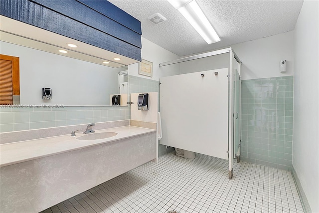 bathroom with tile patterned floors, sink, a textured ceiling, and tile walls