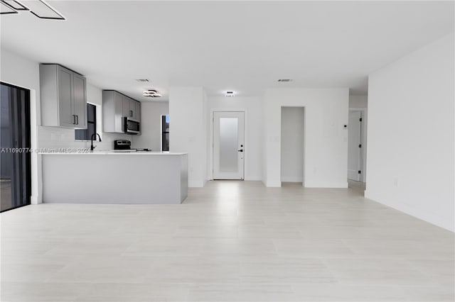 kitchen with sink, kitchen peninsula, tasteful backsplash, range, and gray cabinetry