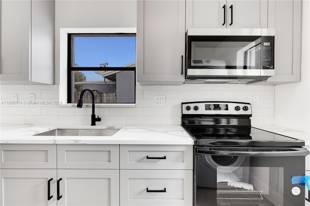 kitchen with stainless steel appliances, white cabinetry, sink, and light stone counters