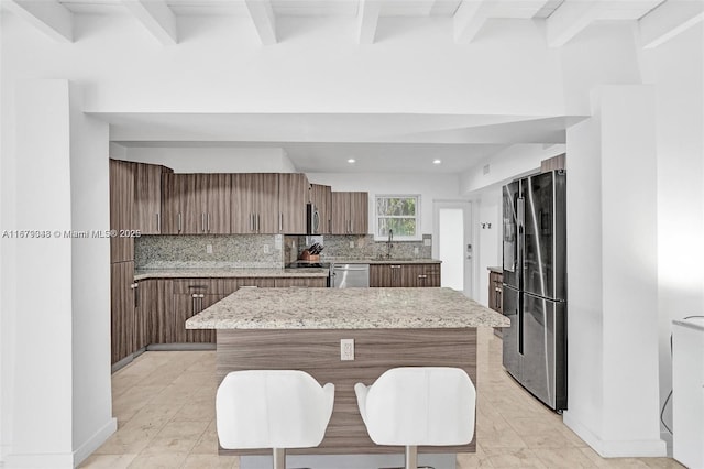 kitchen featuring a center island, sink, stainless steel appliances, tasteful backsplash, and light stone counters