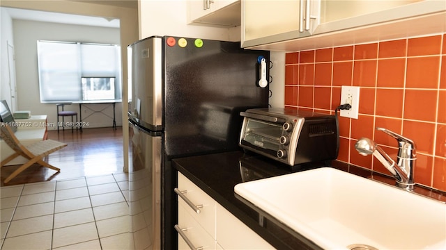 kitchen with tile walls, tile patterned flooring, sink, white cabinetry, and stainless steel fridge