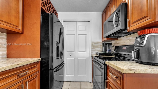 kitchen with black appliances, a textured ceiling, light tile patterned floors, light stone countertops, and decorative backsplash