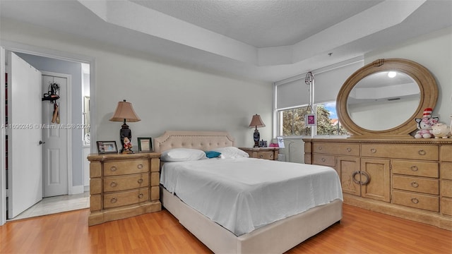 bedroom with light hardwood / wood-style floors, a textured ceiling, and a raised ceiling