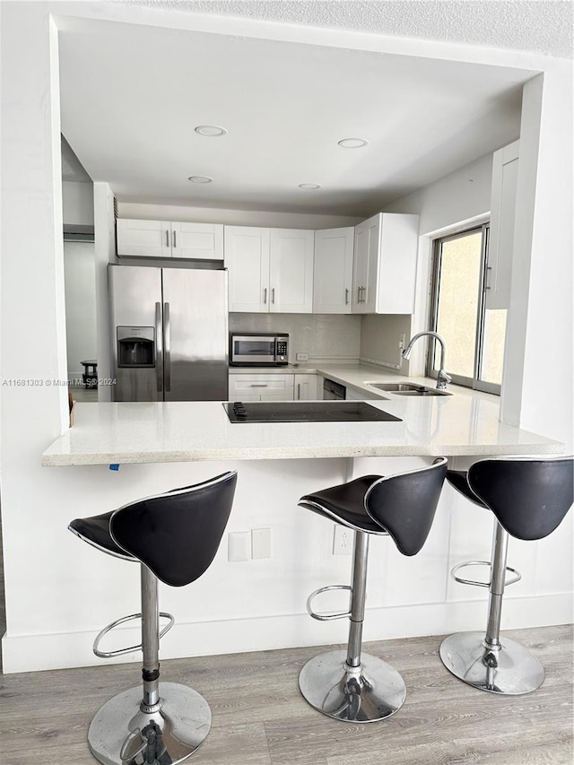 kitchen featuring a kitchen bar, appliances with stainless steel finishes, kitchen peninsula, light hardwood / wood-style flooring, and white cabinetry