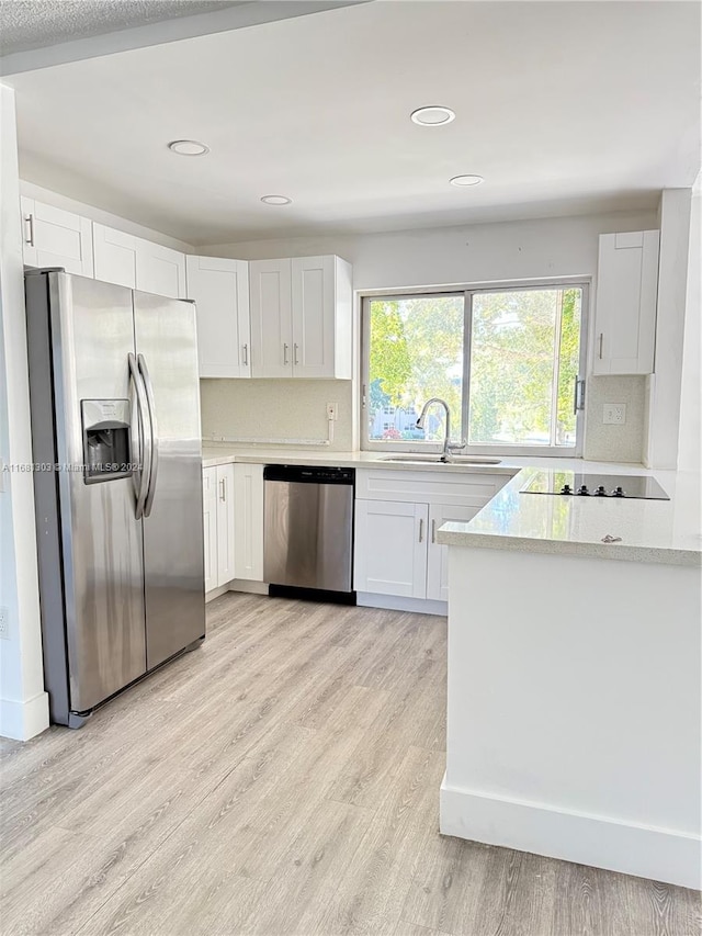 kitchen featuring backsplash, sink, light wood-type flooring, white cabinetry, and stainless steel appliances