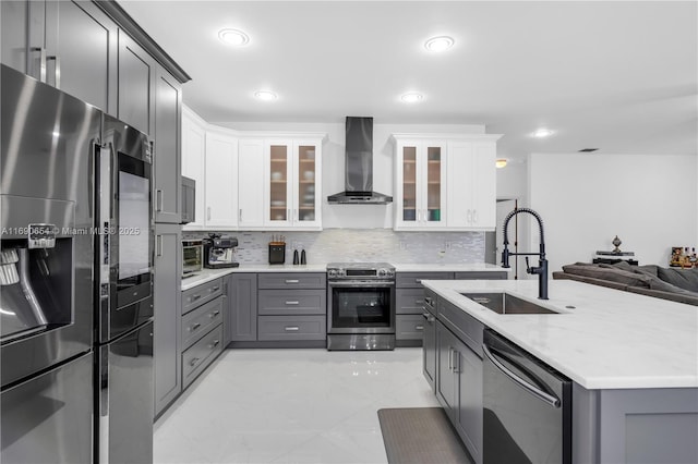 kitchen featuring a sink, appliances with stainless steel finishes, wall chimney range hood, gray cabinets, and backsplash