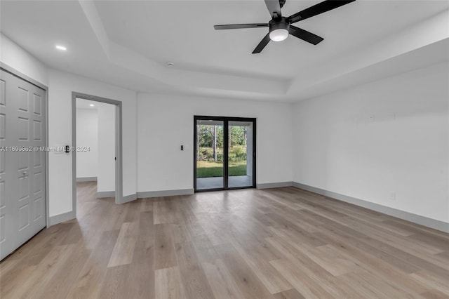 empty room featuring light hardwood / wood-style floors, ceiling fan, and a tray ceiling