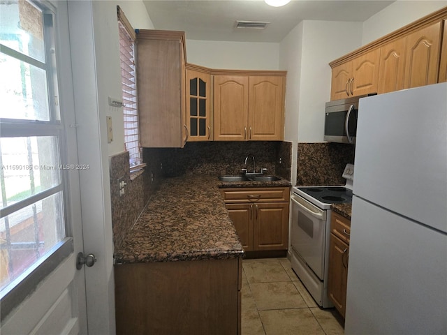 kitchen with sink, backsplash, dark stone counters, white appliances, and light tile patterned floors