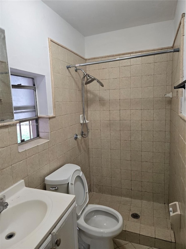 bathroom with a tile shower, vanity, toilet, and tile walls