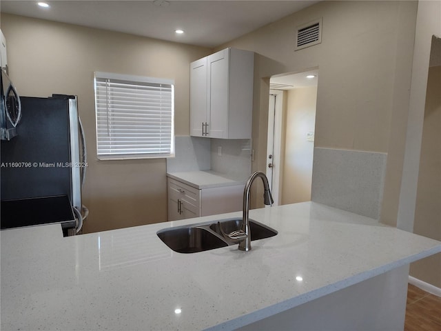 kitchen with light stone countertops, stove, kitchen peninsula, sink, and white cabinets