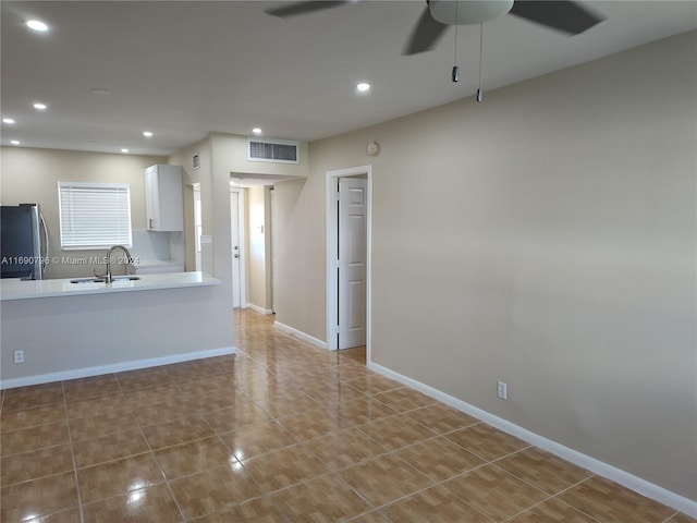 kitchen with stainless steel fridge, tile patterned floors, ceiling fan, sink, and white cabinets