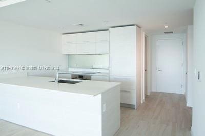 kitchen with white cabinets, an island with sink, light hardwood / wood-style flooring, and sink