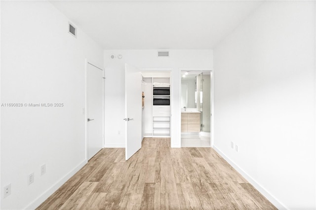 unfurnished bedroom featuring light wood finished floors, visible vents, a spacious closet, and a closet