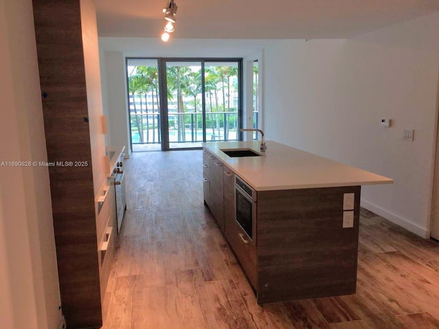 kitchen with sink, oven, an island with sink, and light wood-type flooring