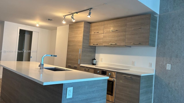 kitchen with sink, a breakfast bar area, stainless steel oven, an island with sink, and black electric stovetop